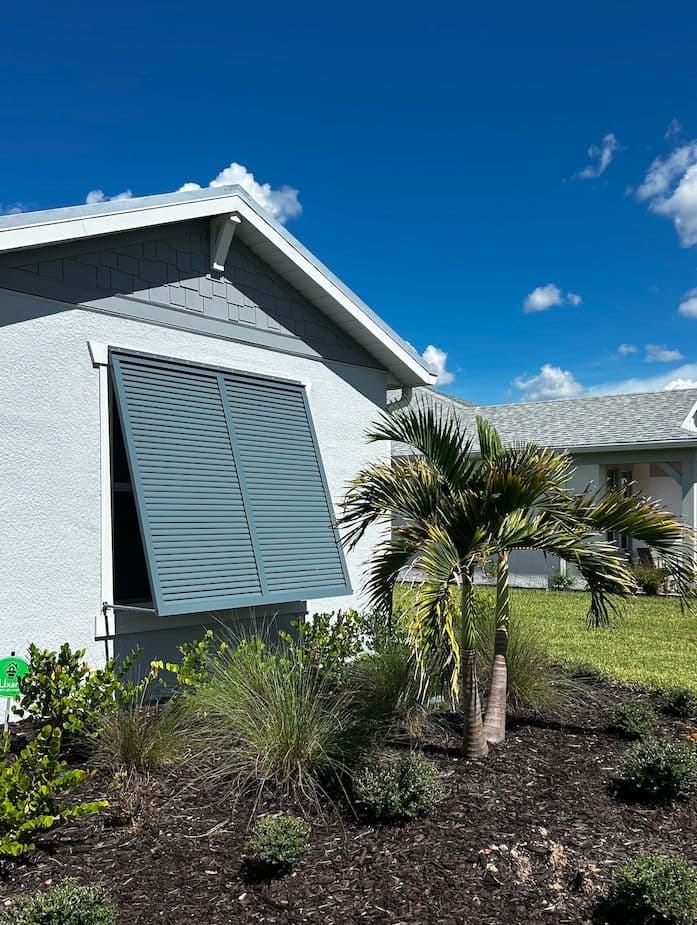Bahama shutter over a window on a blue-gray home