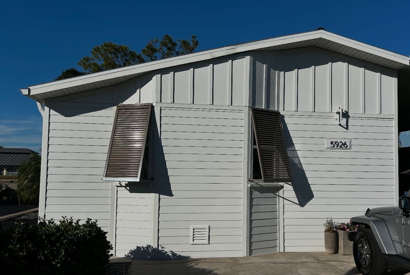 Two Bahama shutters propped open on a gray board-and-batten home