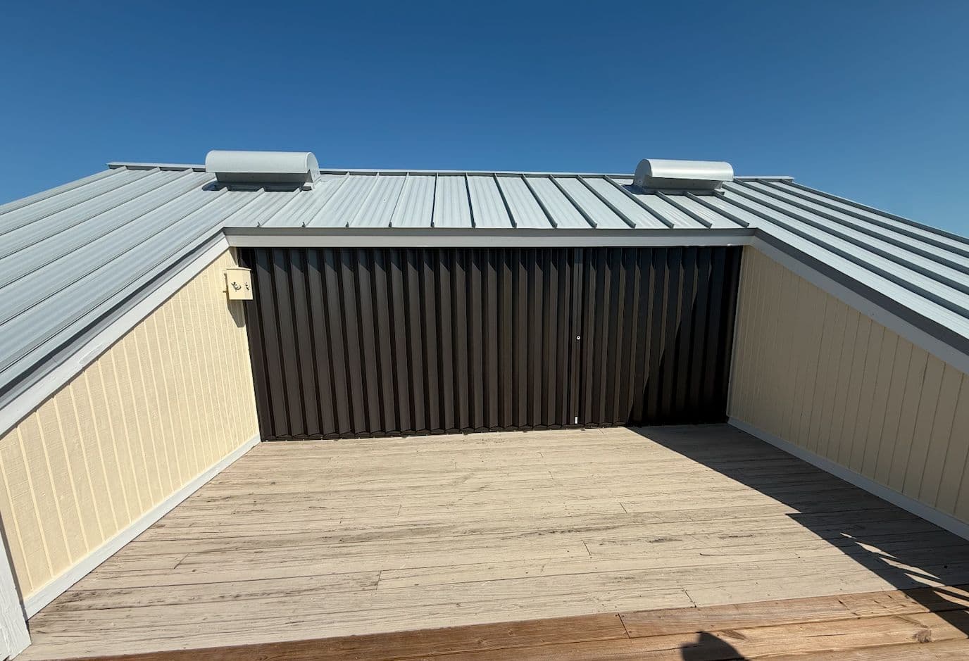 Dark bronze accordion hurricane shutter closed across the opening of a rooftop deck