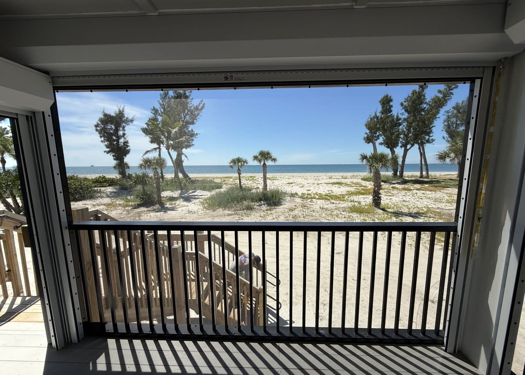 Beach and palms seen through a roll-down screen on an upper lanai