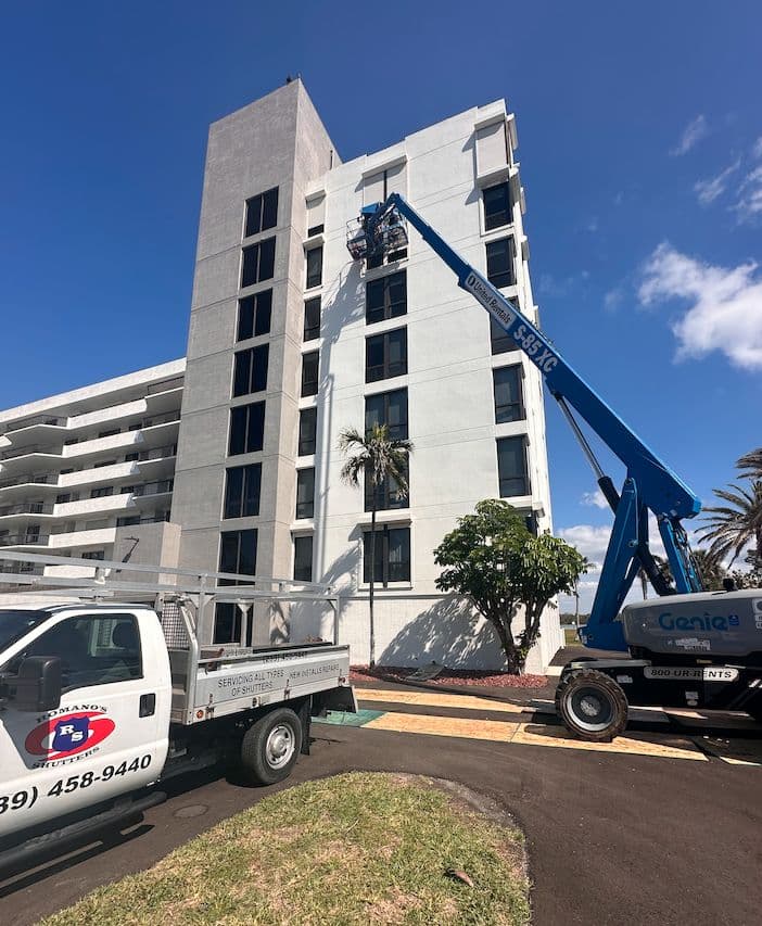 Romano's Shutters truck and a boom lift working on a high-rise building