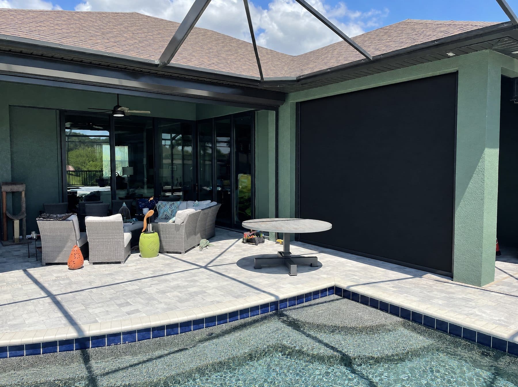 Black roll-down screen lowered across a lanai beside a pool