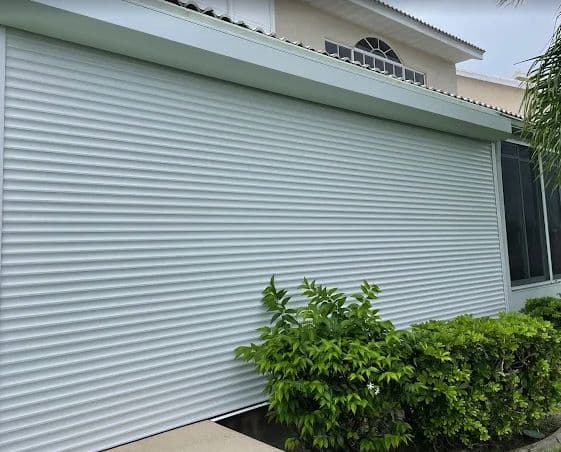 Full-height white roll-down shutter closed across a wall of windows